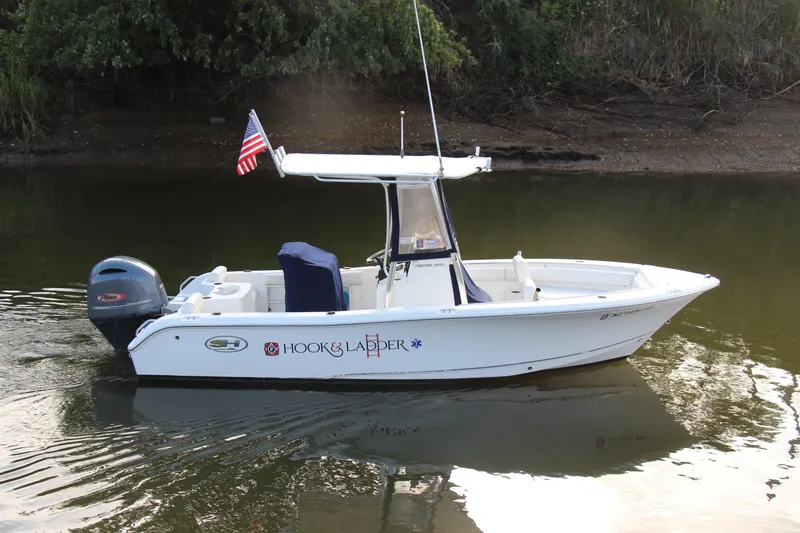 Slide: The Image of 2019 Sea Hunt Triton 210 boat on calm water, featuring an American flag and Yamaha outboard motor. - 0