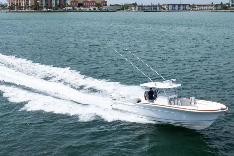 Slide: The Image of 2026 Buddy Davis 34 Center Console cruising on open water near coastal buildings. - 27