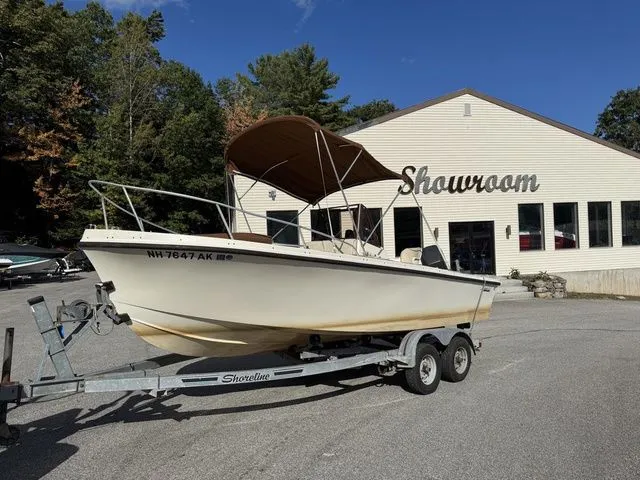 Slide: The Image of 1990 Mako 201 boat on trailer outside showroom, clear sky, trees in background. - 1
