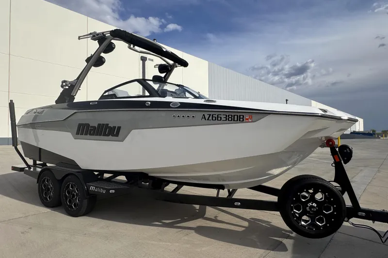 The Image of 2023 Malibu M220 boat on trailer, parked outdoors under cloudy sky. - 0