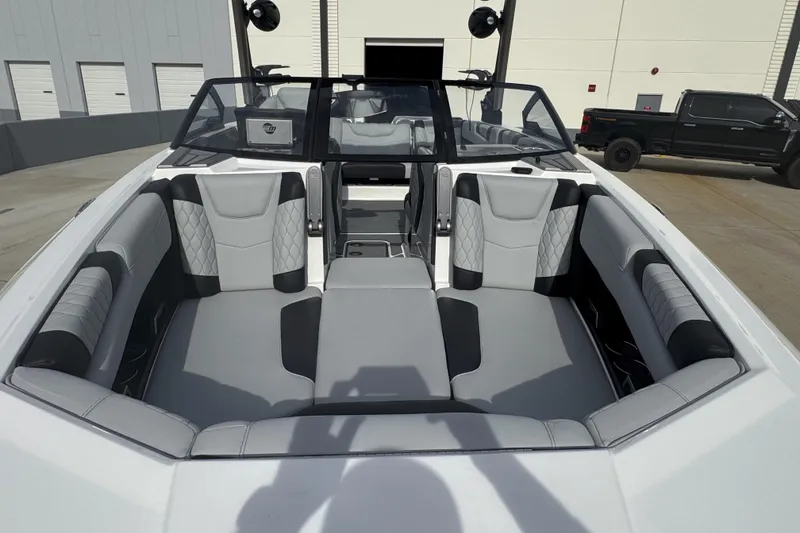 Slide: The Image of 2023 Malibu M220 boat interior with gray and black seating, docked outdoors. - 2