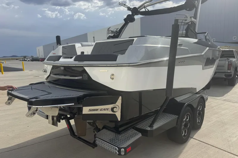 Slide: The Image of 2023 Malibu M220 boat on trailer, featuring Surf Gate technology, parked outdoors. - 6