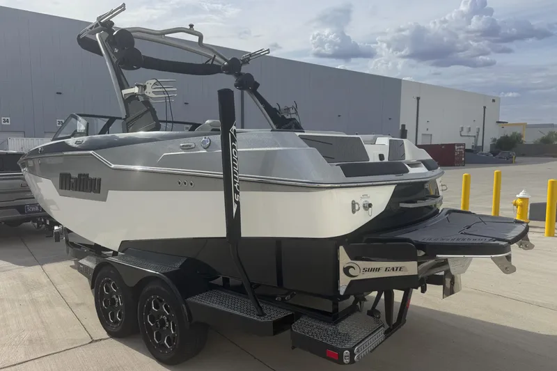 Slide: The Image of 2023 Malibu M220 boat on trailer, parked outdoors near industrial building. - 9