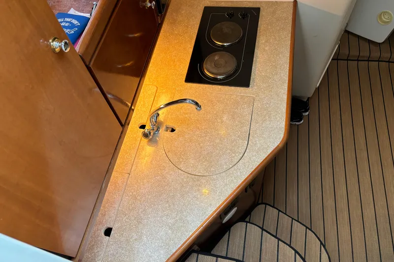 Slide: The Image of 1999 Trojan 320 Express boat interior with kitchenette, featuring a sink and stovetop. - 22