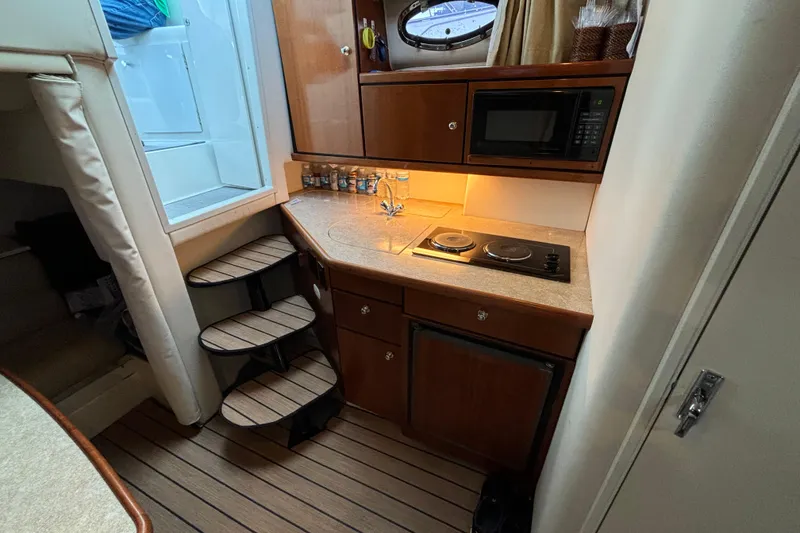Slide: The Image of 1999 Trojan 320 Express yacht interior kitchen with stove, microwave, and wooden cabinetry. - 25