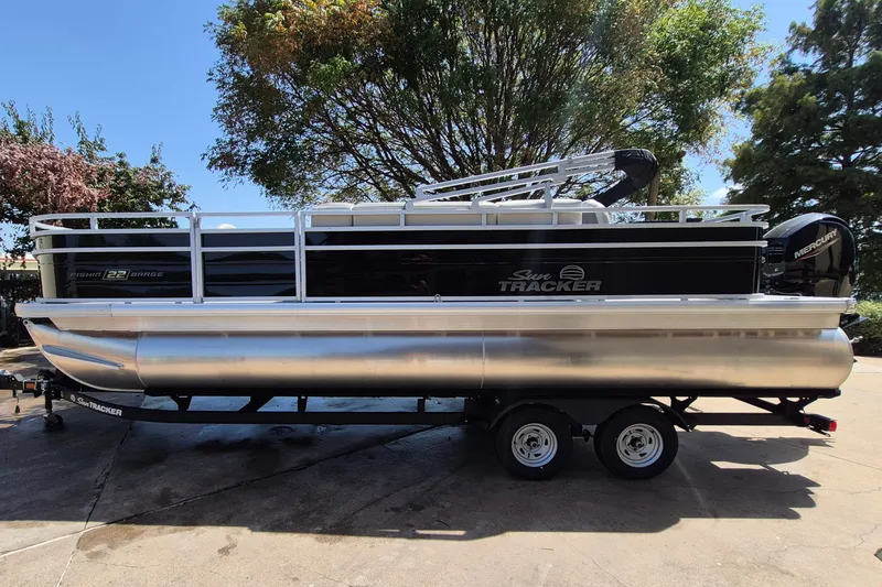 The Image of 2026 Sun Tracker Fishin' Barge 22 DLX pontoon boat on trailer, parked outdoors. - 0