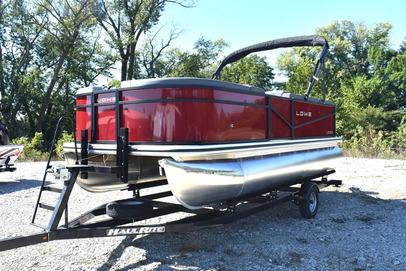 Slide: The Image of 2026 Lowe LS 190 pontoon boat on trailer, parked outdoors with trees in background. - 6