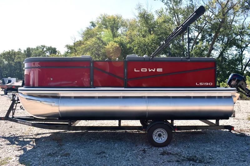 Slide: The Image of 2026 Lowe LS 190 pontoon boat in red, parked on a trailer, surrounded by trees. - 7