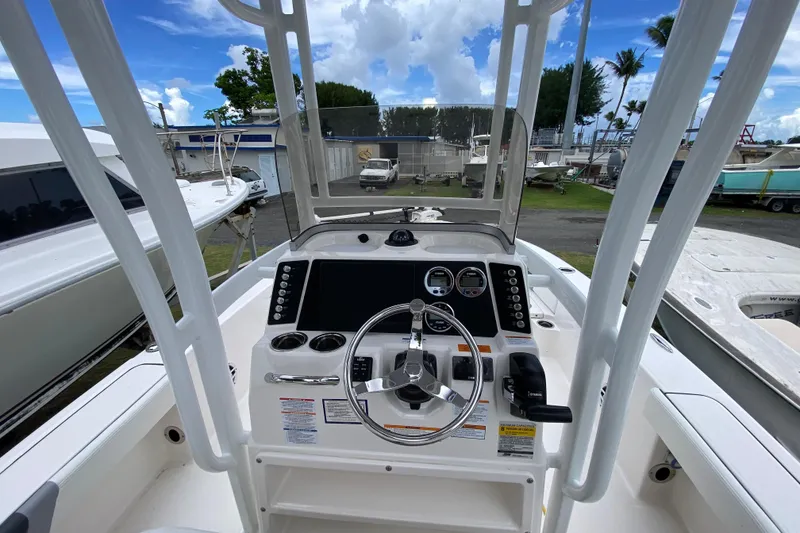 Slide: The Image of 2023 Robalo 226 Cayman boat console with steering wheel and controls, docked outdoors. - 2
