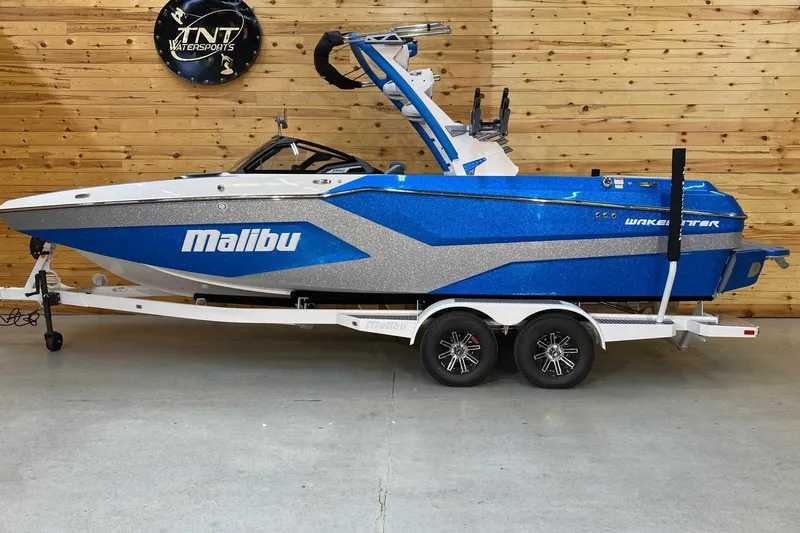 The Image of 2024 Malibu Wakesetter 23 MXZ boat in blue and silver on a trailer indoors. - 1