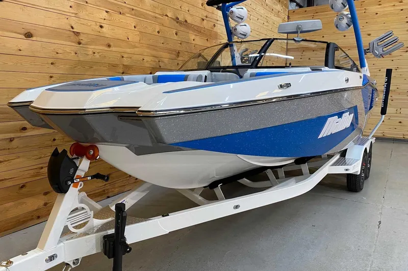 Slide: The Image of 2024 Malibu Wakesetter 23 MXZ boat in showroom, blue and white design, on trailer. - 3