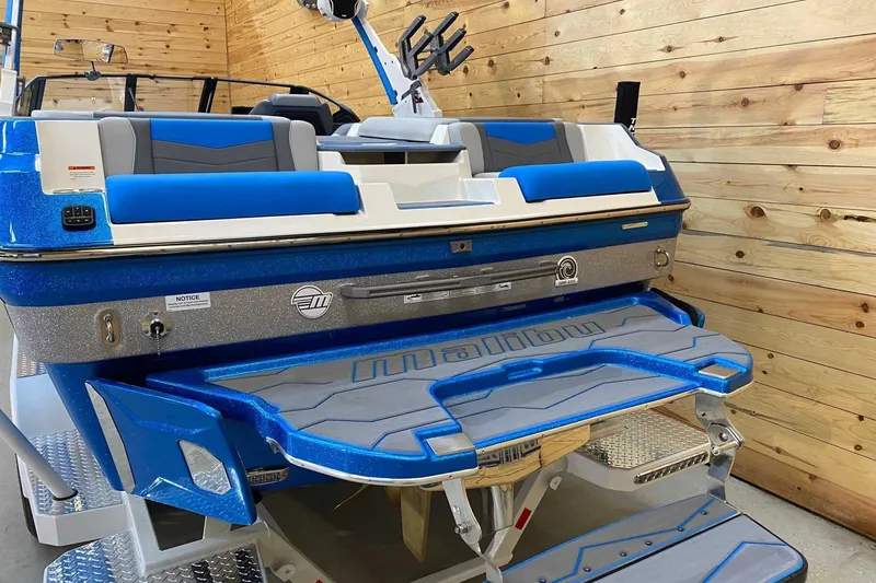 Slide: The Image of 2024 Malibu Wakesetter 23 MXZ boat with blue and gray seating, wooden backdrop. - 4