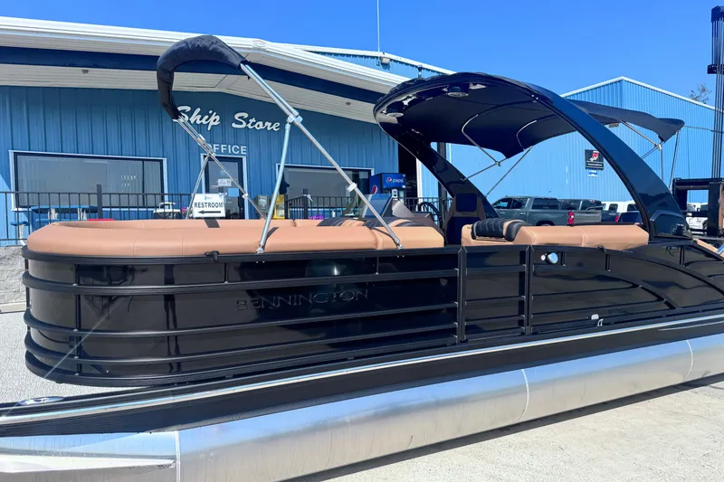 The Image of 2026 Bennington 27RSBAT2 pontoon boat with sleek black design, docked near a blue building. - 0