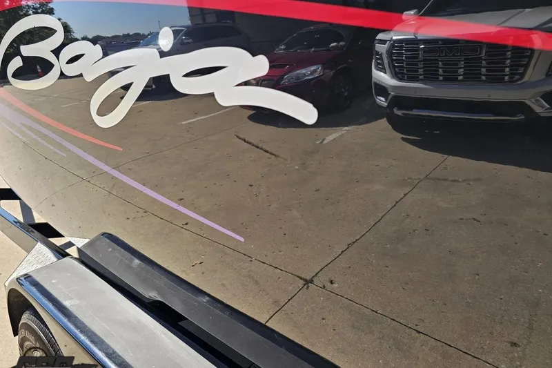 Slide: The Image of 2005 Baja 25 Outlaw boat with logo, parked near vehicles. - 25