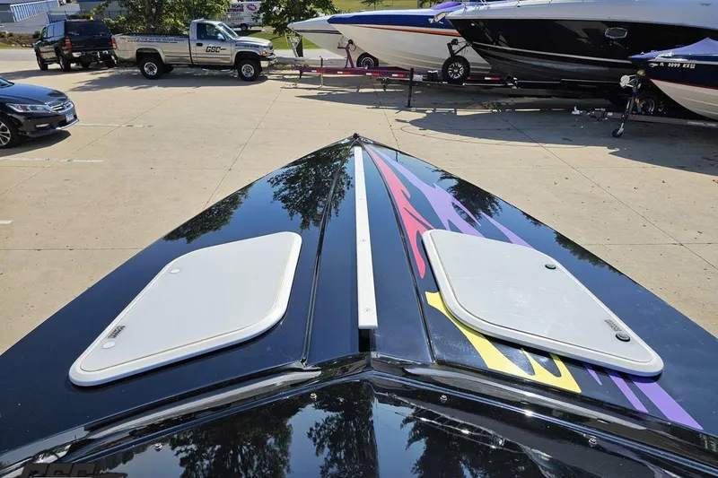 Slide: The Image of 2005 Baja 25 Outlaw boat with vibrant graphics, parked near other vehicles. - 73