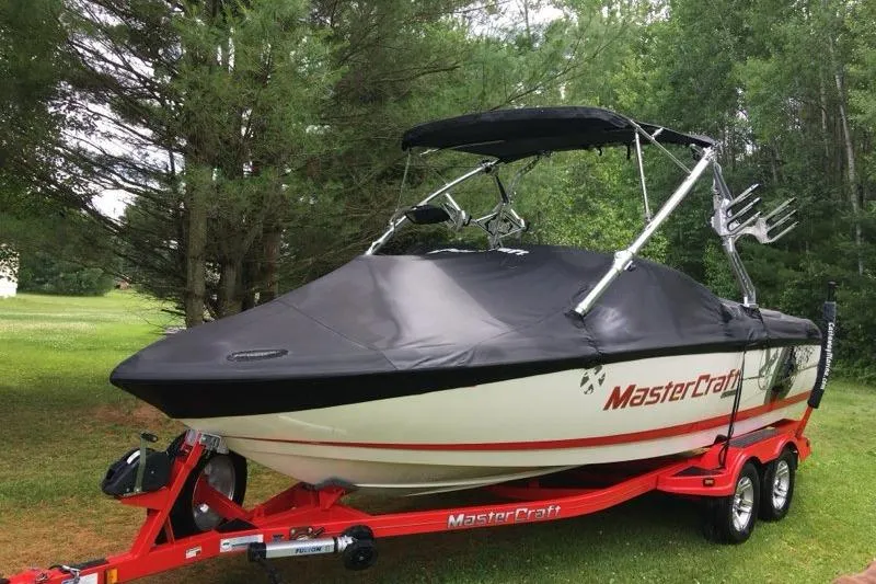 Slide: The Image of 2009 MasterCraft X-15 boat on red trailer, covered, in a wooded area. - 12