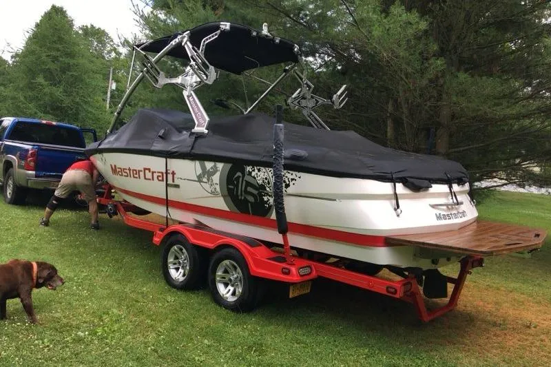 Slide: The Image of 2009 MasterCraft X-15 boat on red trailer, parked on grass with trees in background. - 13
