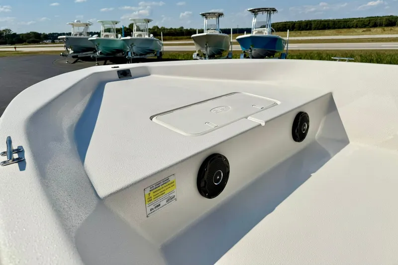 Slide: The Image of 2025 Carolina Skiff EV198 Sea Skiff interior with storage hatch and speakers, parked with other boats. - 10