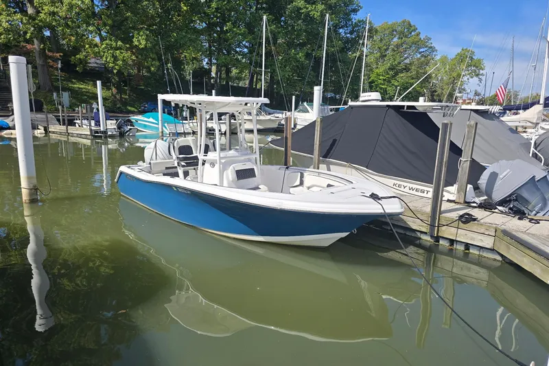 The Image of 2024 Tidewater 220 CC Adventure boat docked in a marina, surrounded by trees and other boats. - 0