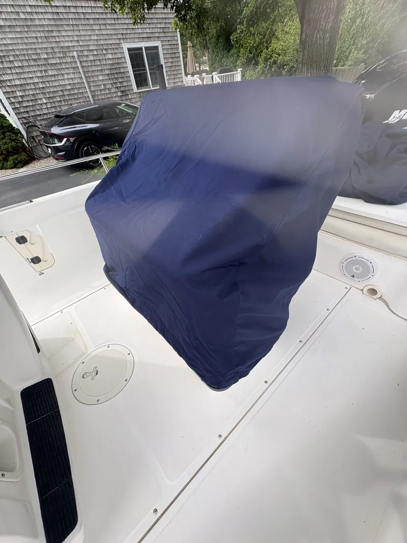 Slide: The Image of 2004 Boston Whaler 220 Dauntless boat interior with blue cover, parked outdoors. - 11