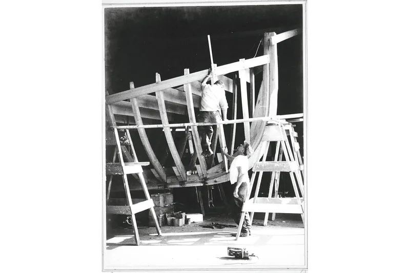 Slide: The Image of 1972 custom tug boat under construction, workers assembling wooden frame in shipyard. - 28