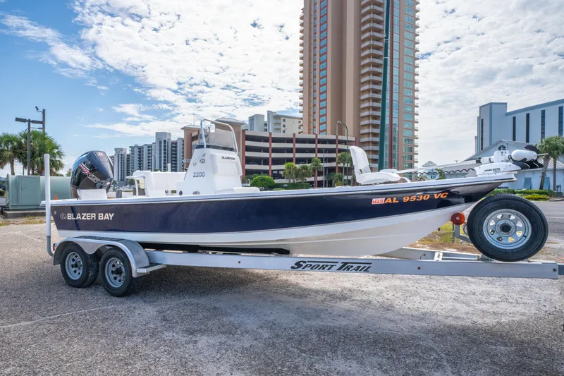 Slide: The Image of 2021 Blazer Bay 2200 boat on trailer, urban backdrop, clear sky. - 0