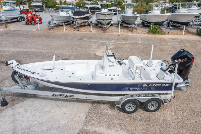 Slide: The Image of 2021 Blazer Bay 2200 boat on trailer, parked in a marina with other boats. - 1
