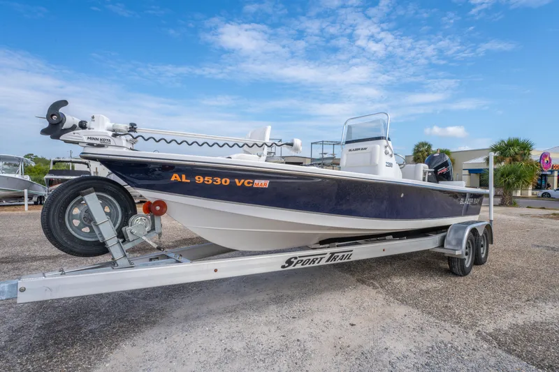 Slide: The Image of 2021 Blazer Bay 2200 boat on trailer, parked outdoors under blue sky. - 2