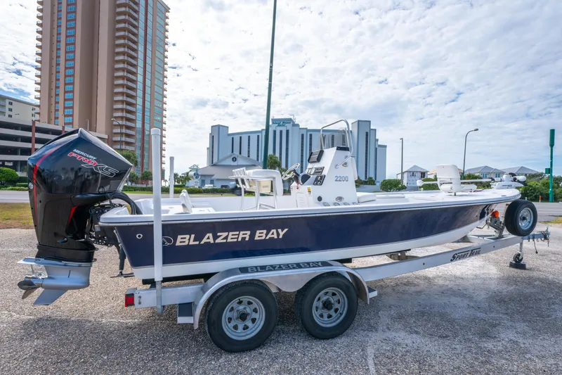 Slide: The Image of 2021 Blazer Bay 2200 boat on trailer, parked near tall buildings under a cloudy sky. - 4