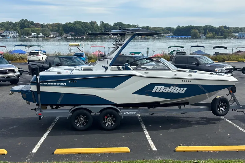Slide: The Image of 2025 Malibu Wakesetter 22 MXZ boat on trailer by a lakeside parking lot. - 8