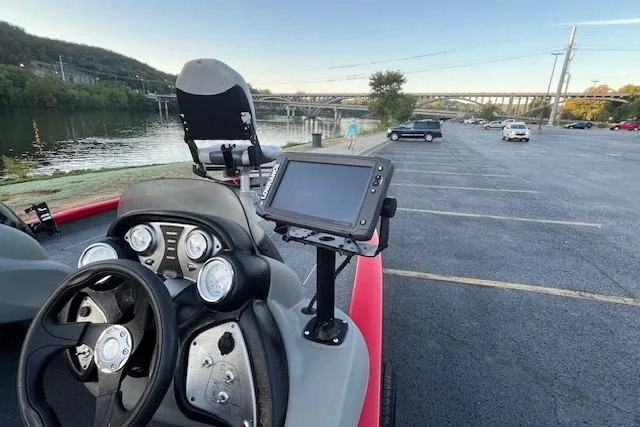 Slide: The Image of 2016 Tracker Pro Team 175 TXW boat interior with seating and control panel by a lake. - 11