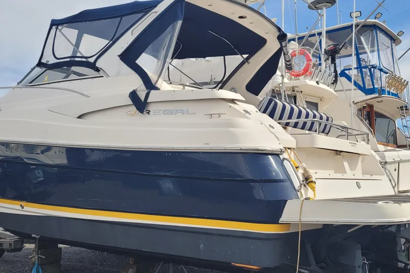 Slide: The Image of 2005 Regal Commodore 3560 IO boat with blue and white exterior, docked at a marina. - 2