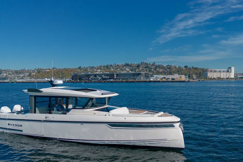 Slide: The Image of 2026 Saxdor 340 GTWA boat cruising on a sunny day near a coastal cityscape. - 1