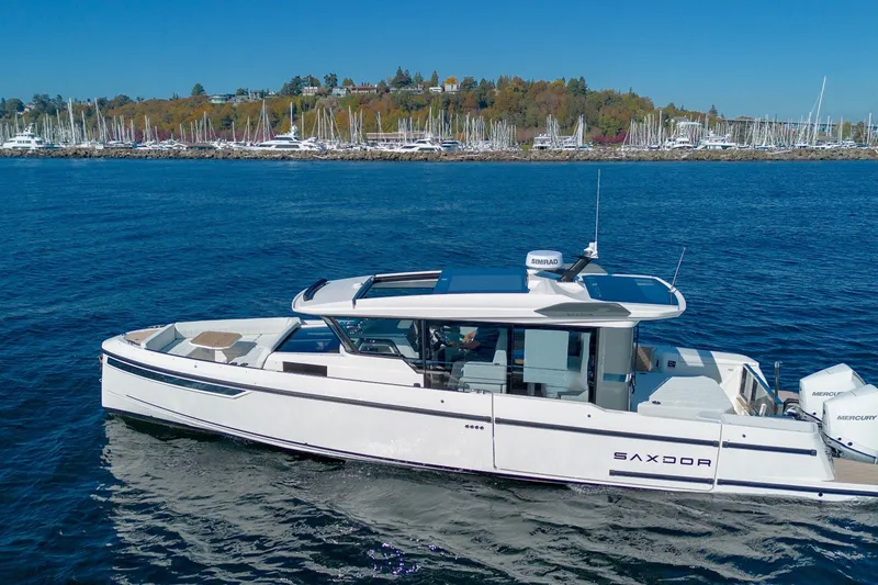 Slide: The Image of 2026 Saxdor 340 GTWA boat cruising on a scenic lake with marina backdrop. - 2