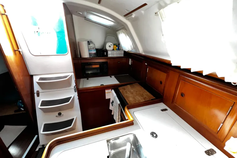 Slide: The Image of Interior of 2002 Beneteau 331 sailboat, featuring a compact kitchen with wood cabinetry. - 34