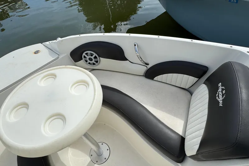 Slide: The Image of 2018 Stingray 204 LR boat interior with seating and table, docked on calm water. - 17