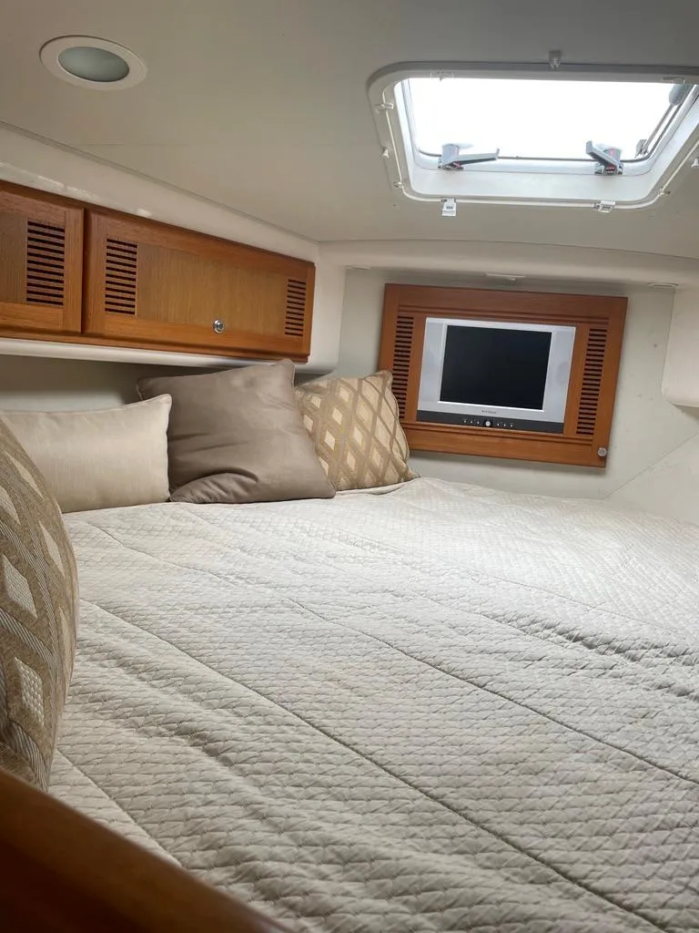 Slide: The Image of 2004 Cabo 35 Express cabin interior with bed, pillows, and small TV. - 31