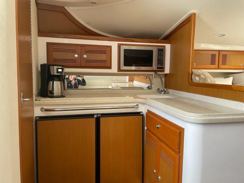 Slide: The Image of 2004 Cabo 35 Express yacht interior with kitchenette, featuring microwave, coffee maker, and wooden cabinetry. - 36