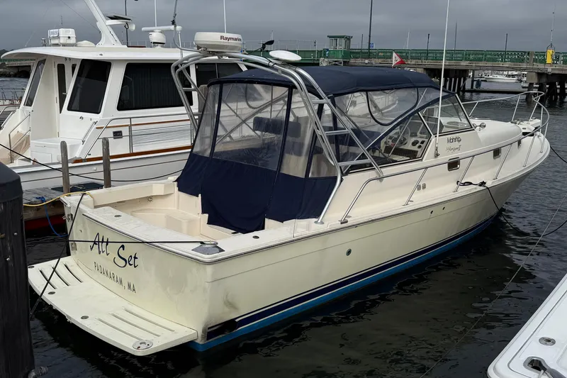 The Image of 2005 Mainship Pilot 34 docked at marina, featuring sleek design and blue canopy. - 0