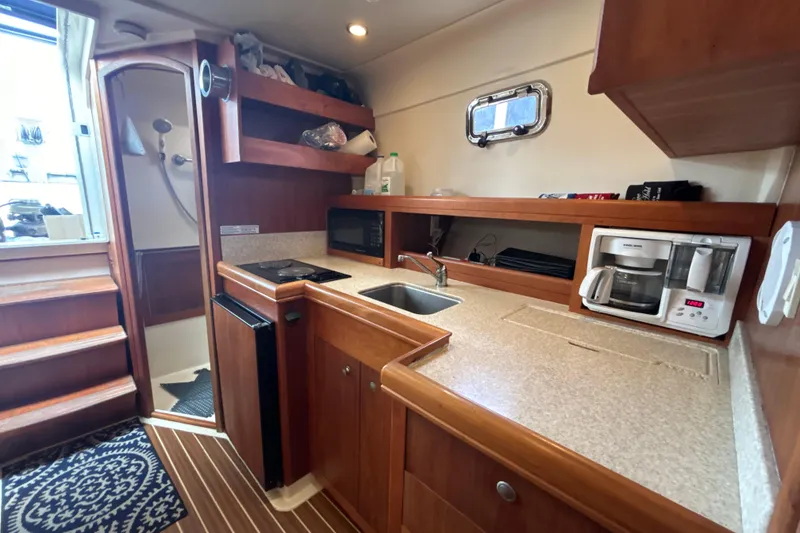 Slide: The Image of 2005 Mainship Pilot 34 galley with sink, stove, microwave, and wooden cabinetry. - 20