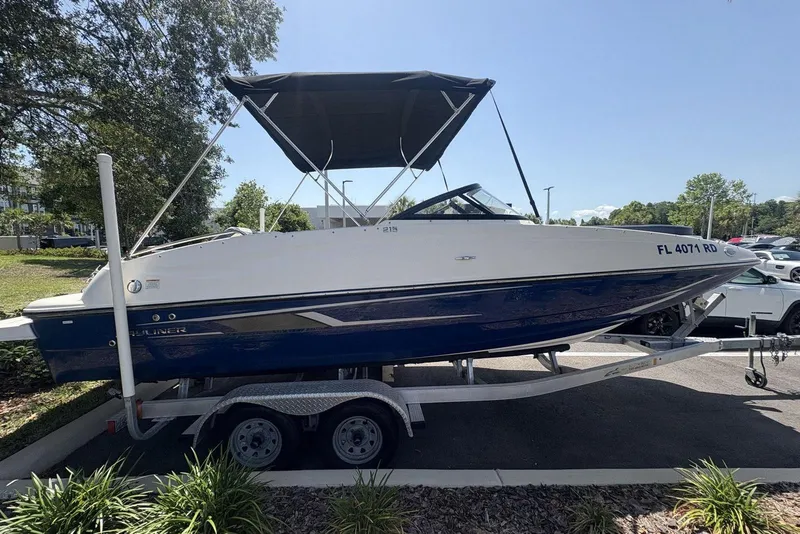 The Image of 2016 Bayliner 215 Deck Boat on trailer, parked outdoors under clear sky. - 0
