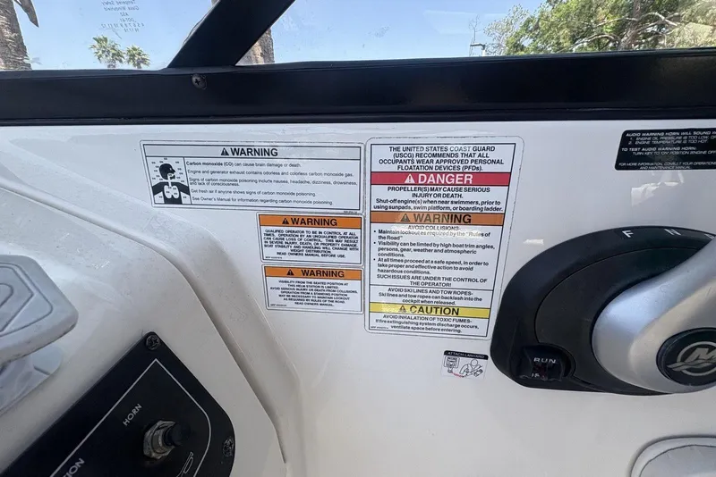 Slide: The Image of 2016 Bayliner 215 Deck Boat dashboard with safety warning labels and control panel. - 20
