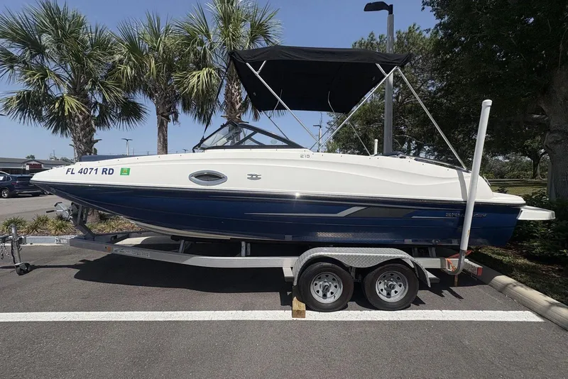 Slide: The Image of 2016 Bayliner 215 Deck Boat on trailer, parked under palm trees. - 3