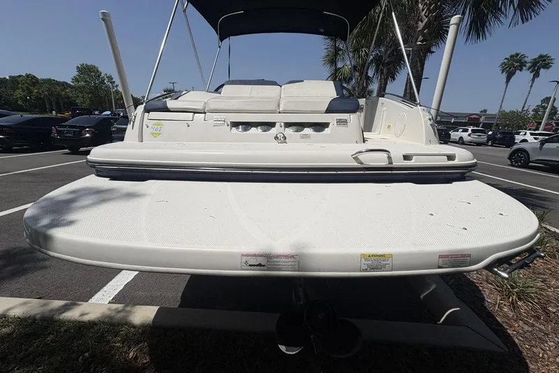Slide: The Image of 2016 Bayliner 215 Deck Boat rear view in parking lot, featuring swim platform and canopy. - 4