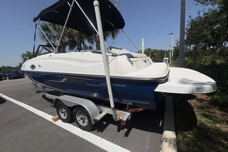 Slide: The Image of 2016 Bayliner 215 Deck Boat on trailer, parked outdoors under a clear sky. - 5