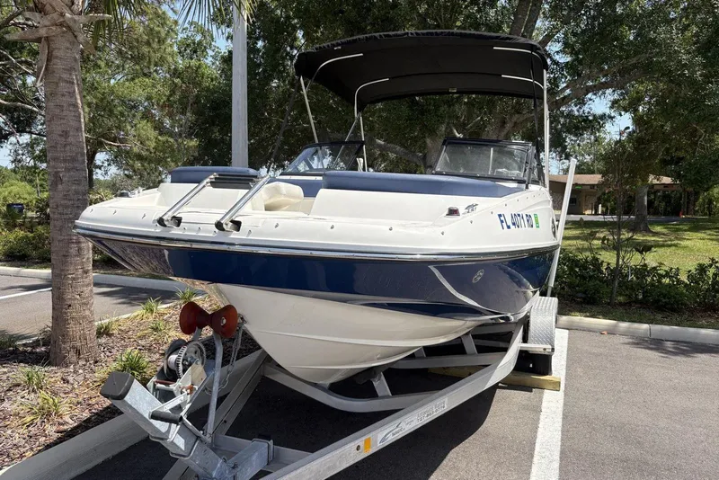 Slide: The Image of 2016 Bayliner 215 Deck Boat on trailer, parked under trees. - 8
