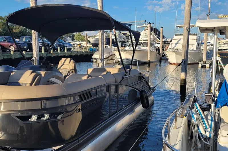 Slide: The Image of 2024 Bennington 24LXSSB pontoon boat docked at a marina under a clear blue sky. - 2
