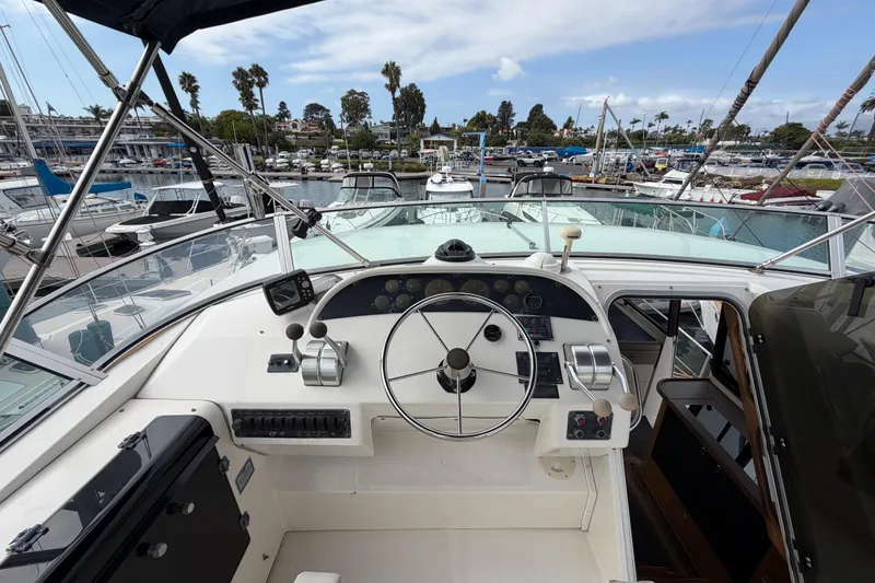 Slide: The Image of 1998 Bayliner 4788 Pilot House Motoryacht helm with marina view, featuring steering wheel and controls. - 46