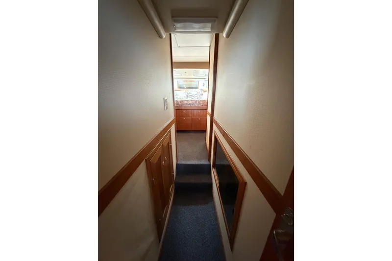 Slide: The Image of Narrow hallway inside 1998 Bayliner 4788 Pilot House Motoryacht, featuring wooden cabinetry and carpeted flooring. - 56