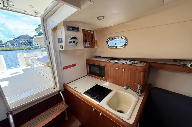 Slide: The Image of 2007 Mainship Pilot 30 Sedan interior with kitchenette, sink, and microwave, overlooking water. - 13